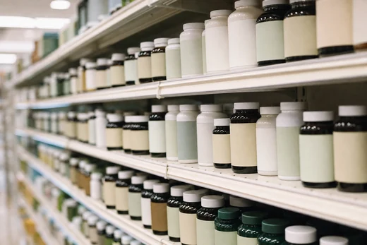 A supermarket vitamin aisle receding into shallow focus, hundreds of unlabelled bottles.